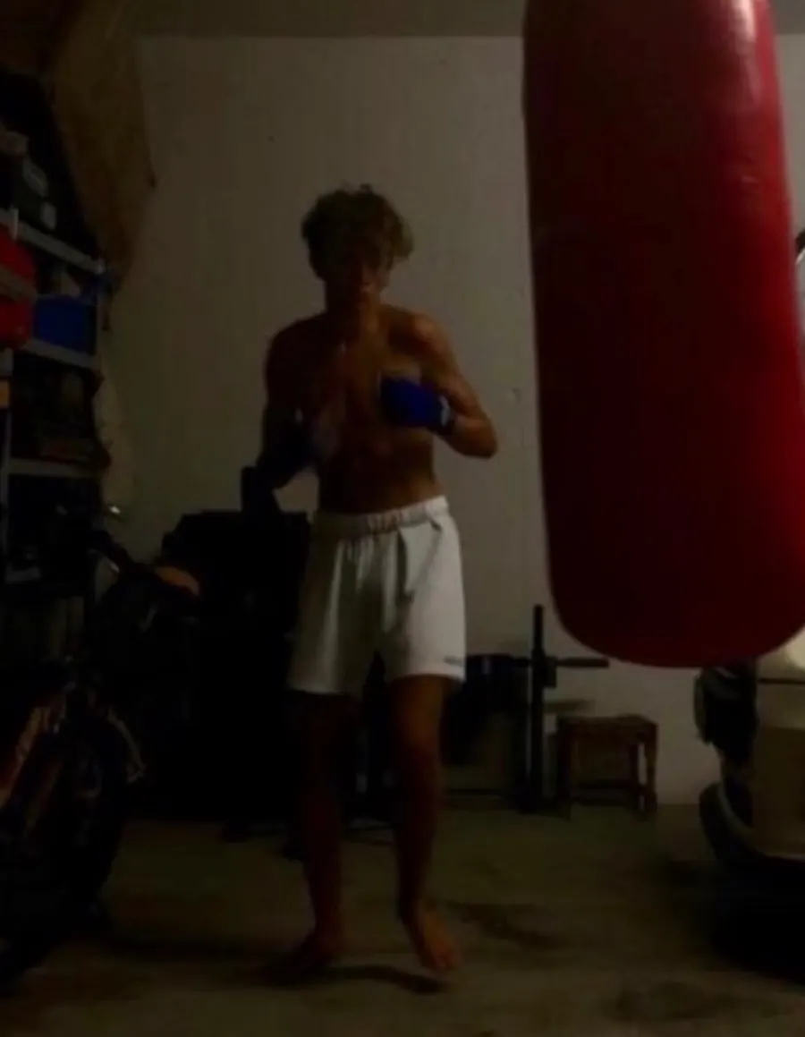 A teenage Gio boxing in a dim home garage next to a heavy bag.
