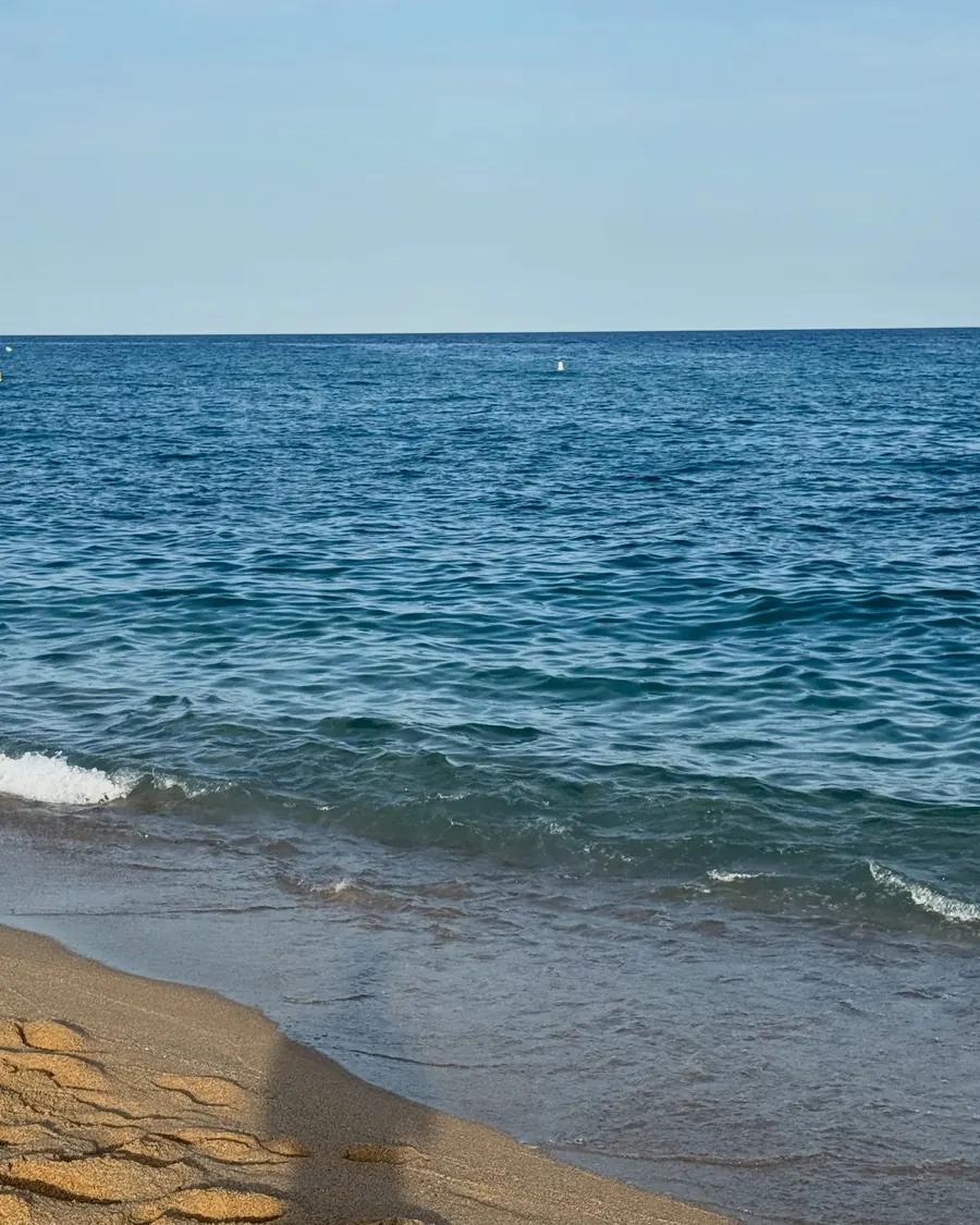 Calm blue Mediterranean sea meeting a sandy beach under a pale sky
