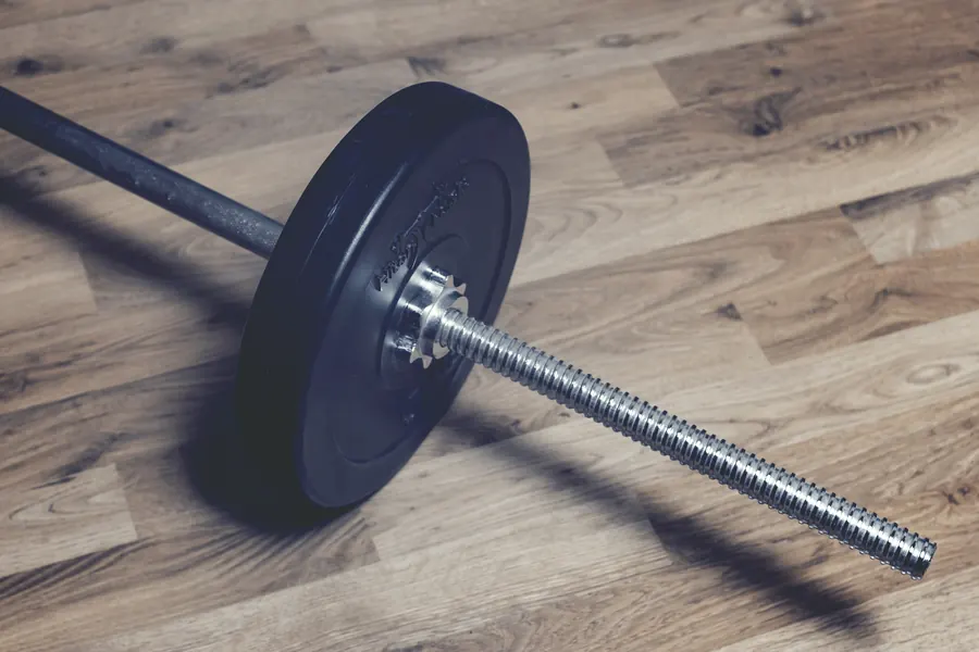 Close-up of a barbell with a single plate resting on a warm wooden floor
